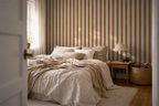 Cozy bedroom with striped yellow wallpaper, bed, lamp, and basket.