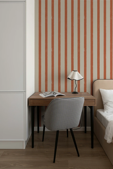 Small desk with chair against a wall with orange and white striped wallpaper.