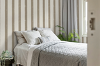 Neatly made bed with decorative pillows against a striped wall with greige striped wallpaper.