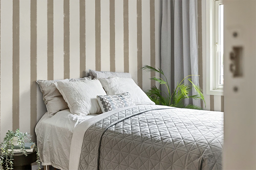 Neatly made bed with decorative pillows against a striped wall with greige striped wallpaper.