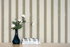 Vase with flowers and books on a wooden surface against a wall with greige striped wallpaper.