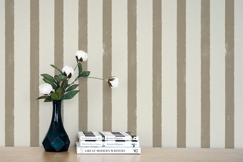 Vase with flowers and books on a wooden surface against a wall with greige striped wallpaper.