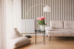 Modern living room with a beige sofa, floor lamp, a small table with flowers, and textured grey striped wallpaper. 