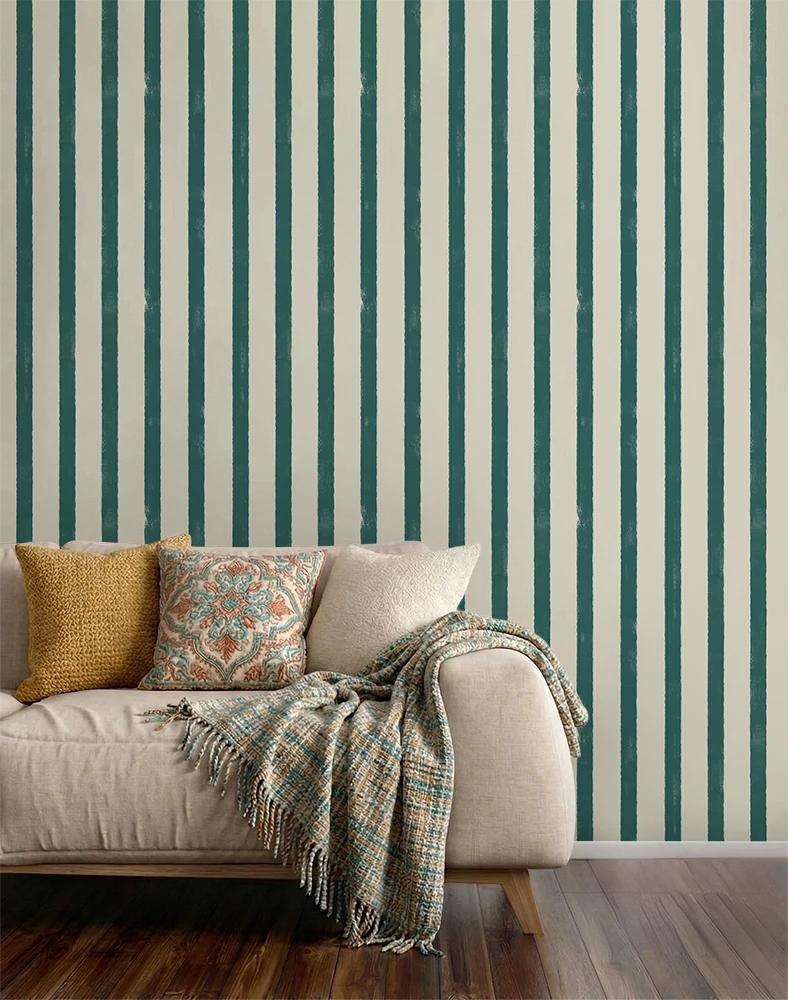 Sofa with decorative pillows and a blanket against a wall with blue striped wallpaper.