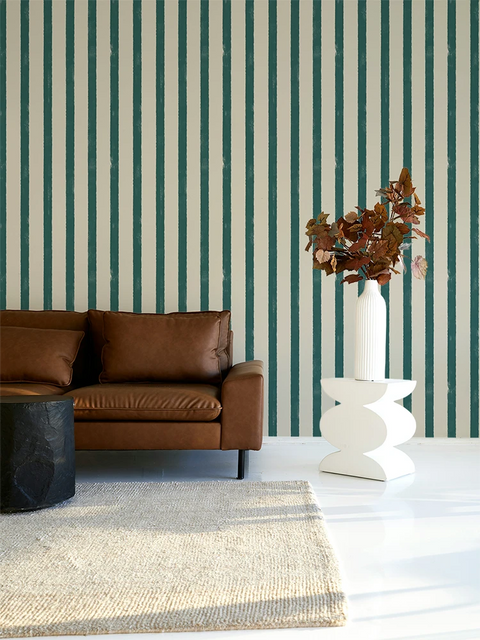 Living room with brown leather sofa, white side table, and striped green and white wallpaper.