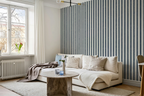 A styled living room corner featuring a cream-colored sectional sofa with neutral throw pillows, a round stone coffee table, and a prominent blue and white vertically striped wallpaper on the accent wall.
