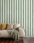 A styled living room corner featuring a beige sofa with decorative pillows and a fringed throw blanket, set against a wall with vertical sage green and off-white striped wallpaper and dark wood flooring.