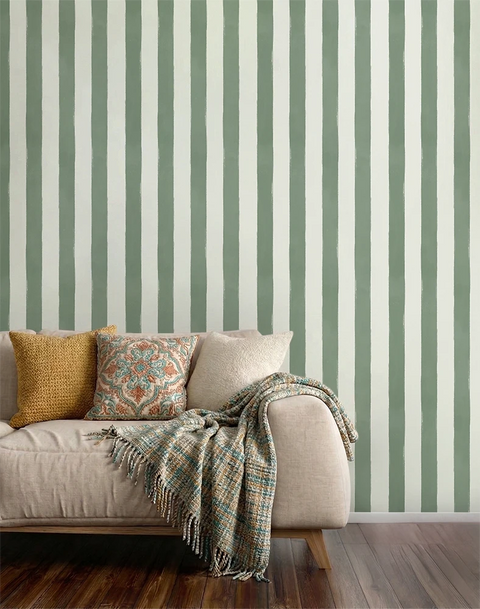 A styled living room corner featuring a beige sofa with decorative pillows and a fringed throw blanket, set against a wall with vertical sage green and off-white striped wallpaper and dark wood flooring.