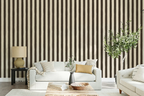 A styled living room featuring a prominent wall with vertical dark brown and beige stripes, decorated with a white sofa, a wooden coffee table, a side table with a lamp, and a potted green tree.