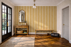 Modern hallway with a bench, side table, mirror, and a striped wallpaper with stripes of cream and yellow. 