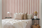 Bedroom with white sheets, a wooden floor, nightstand with a lamp, and a striped wallpaper with pink brush strokes. 