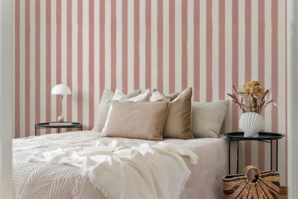Bedroom with white sheets, a wooden floor, nightstand with a lamp, and a striped wallpaper with pink brush strokes. 
