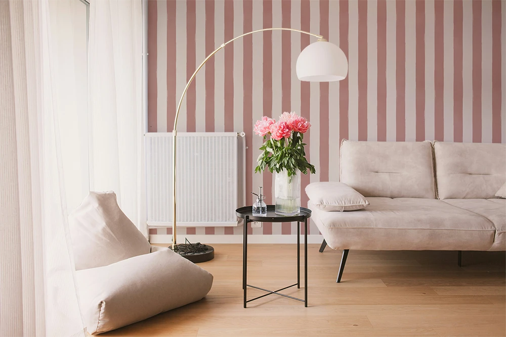 Modern living room with a beige sofa,  a lamp, and a striped wallpaper with pink brush strokes. 