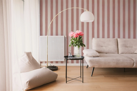 Modern living room with a beige sofa,  a lamp, and a striped wallpaper with pink brush strokes. 