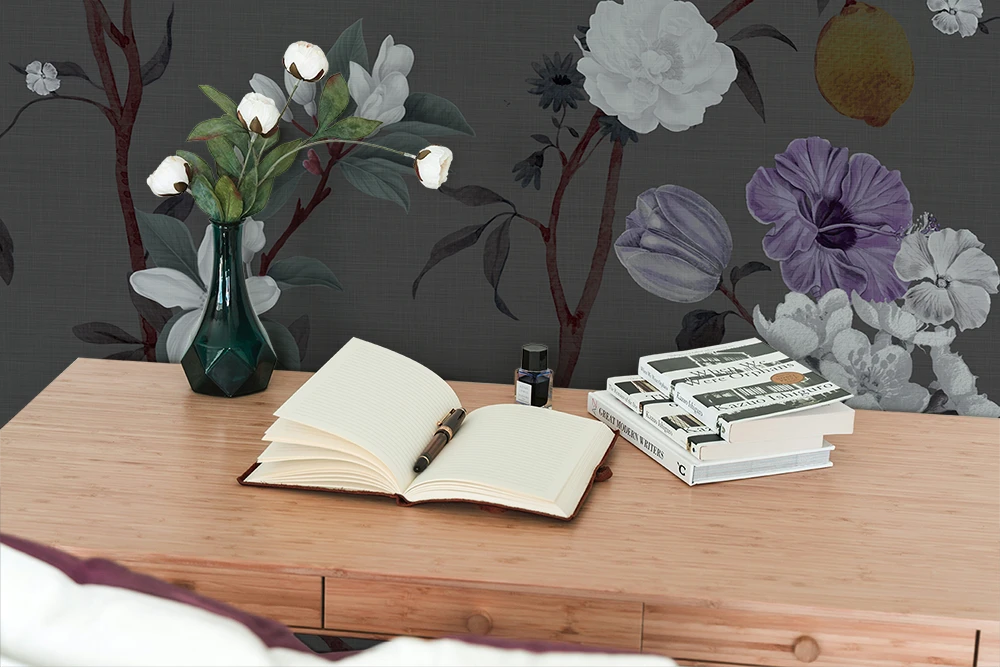 Open book on a wooden desk with stationery items, with chinoiserie wallpaper on the wall. 