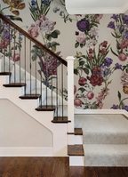 A staircase interior with dark wood steps and a white handrail, set against a wall covered in large floral wallpaper. The wallpaper features a dense botanical pattern with pink, purple, blue, and green flowers and leaves on a light background.