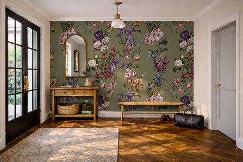 A styled interior room featuring a prominent olive green floral wallpaper with pink, purple, and white botanical patterns on the back wall. The room includes a wooden console table with a mirror, a wooden bench, a black leather bag on the floor, a patterned rug, and a light wood herringbone floor.