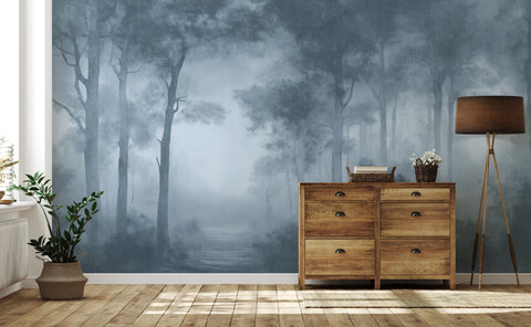 A room interior featuring a large wallpaper mural of a misty blue-gray forest with tall trees. In front of the wall is a wooden six-drawer cabinet, a floor lamp, and a potted plant on a light wood floor.