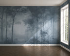 A large wallpaper mural depicting a misty blue-gray forest with tall trees and soft sunlight streaming through, shown installed on a room wall above a wood herringbone floor next to a white window.