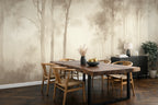 A dining room scene featuring a large wallpaper mural with a misty forest tree pattern in muted beige and brown tones. The room is furnished with a rectangular wooden dining table and four wooden chairs, with a dark sideboard, lamp, and potted plant against the wall.