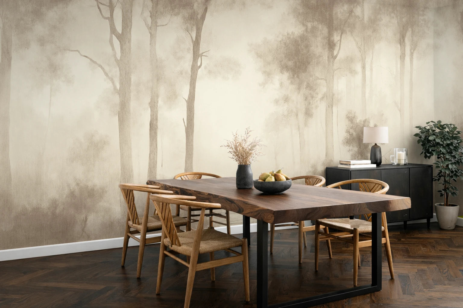 A dining room scene featuring a large wallpaper mural with a misty forest tree pattern in muted beige and brown tones. The room is furnished with a rectangular wooden dining table and four wooden chairs, with a dark sideboard, lamp, and potted plant against the wall.