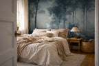 A styled bedroom interior featuring a large forest mural wallpaper on the back wall behind a bed with beige linens, a wooden nightstand with a lamp, and a woven basket on the floor.