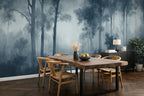 A dining room featuring a large wallpaper2 mural of a misty blue forest with tall trees. In front of the wall is a rustic wooden dining table with six light wood chairs.