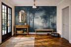 A styled entryway featuring a large wallpaper mural with a misty forest scene in deep blue and gray tones. The room has warm wood floors, a wooden console table with an arched mirror, a bench, and a black duffel bag on the floor.
