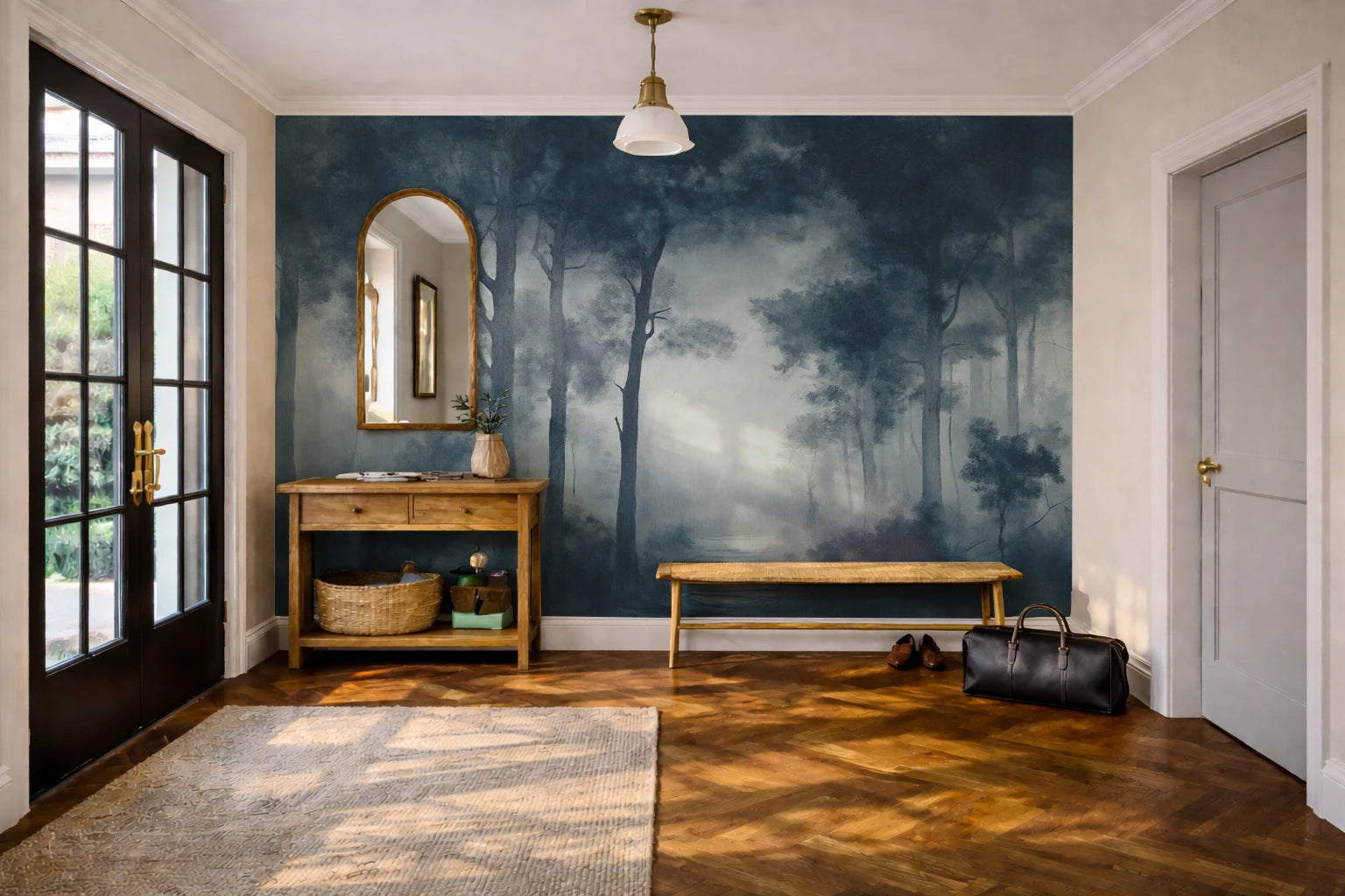 A styled entryway featuring a large wallpaper mural with a misty forest scene in deep blue and gray tones. The room has warm wood floors, a wooden console table with an arched mirror, a bench, and a black duffel bag on the floor.