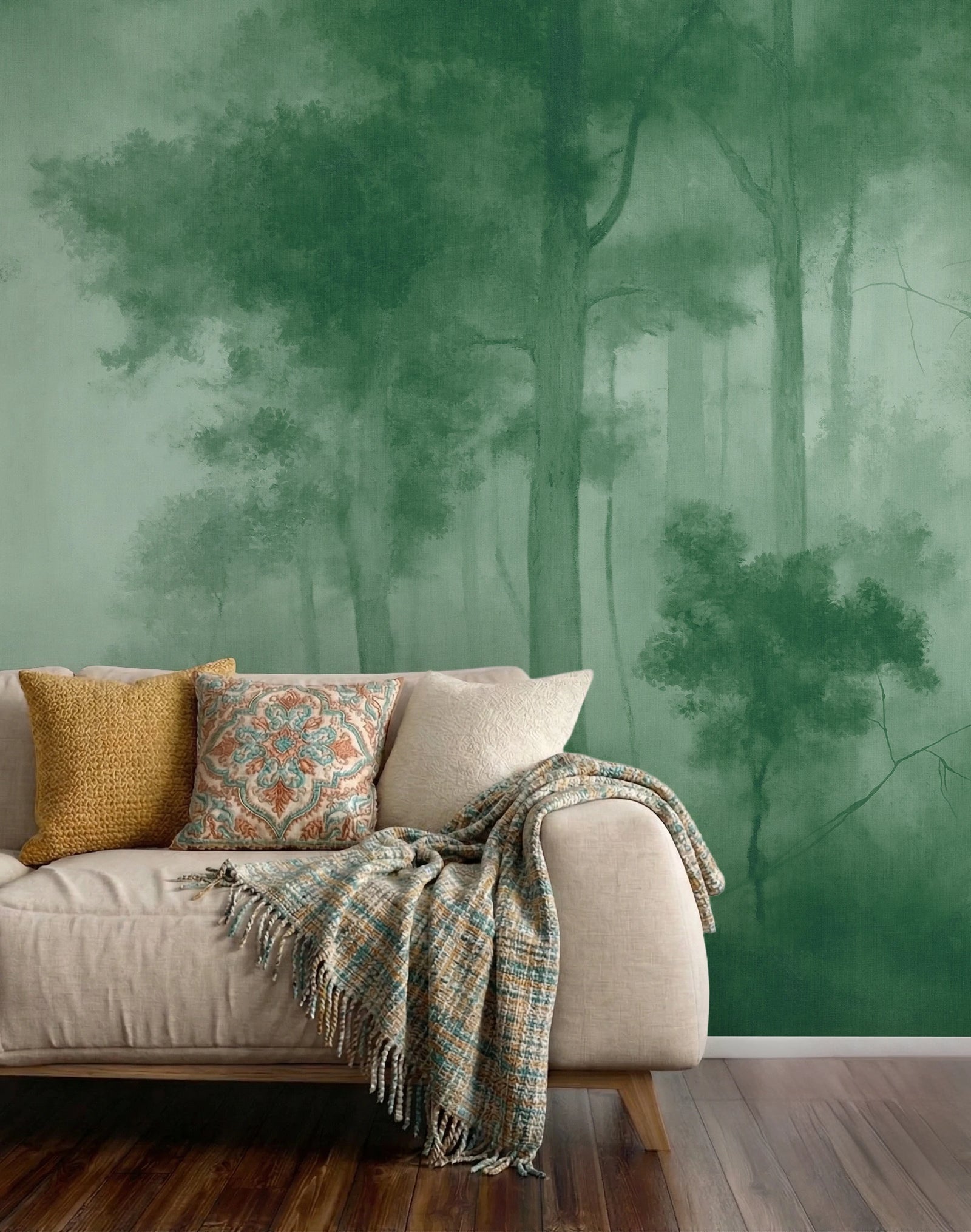 A living room scene featuring a large wallpaper mural of a misty green forest, styled with a beige sofa, patterned pillows, and a fringed throw blanket on a dark wood floor.