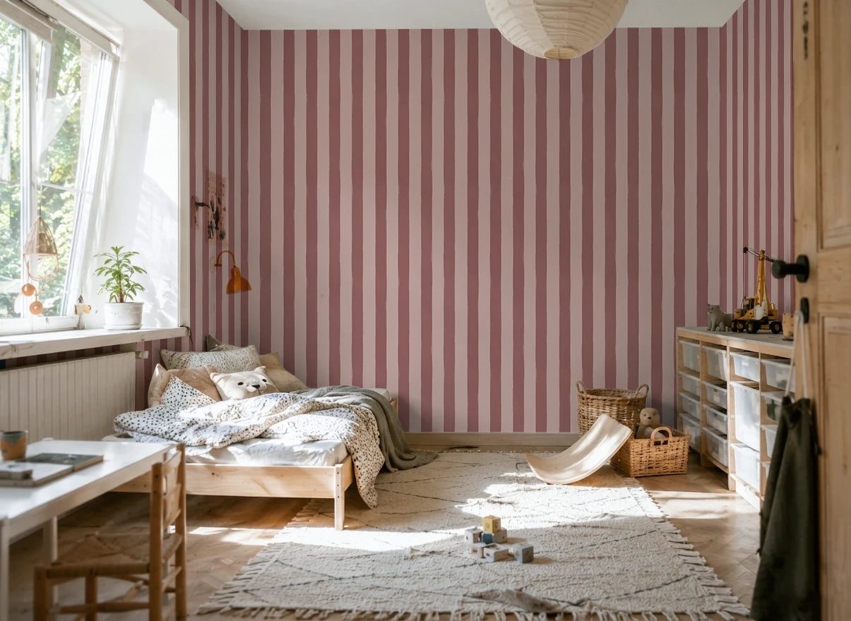 A styled bedroom interior featuring prominent vertical pink striped wallpaper on the main wall, with a wooden bed, light-colored rug, storage cabinet, and window on the left.