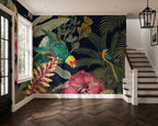 A large tropical jungle wallpaper mural featuring colorful parrots, palm leaves, and hibiscus flowers on a dark navy background, shown in a modern interior with a staircase and wood herringbone floor.