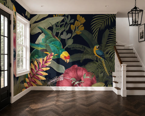 A large tropical jungle wallpaper mural featuring colorful parrots, palm leaves, and hibiscus flowers on a dark navy background, shown in a modern interior with a staircase and wood herringbone floor.