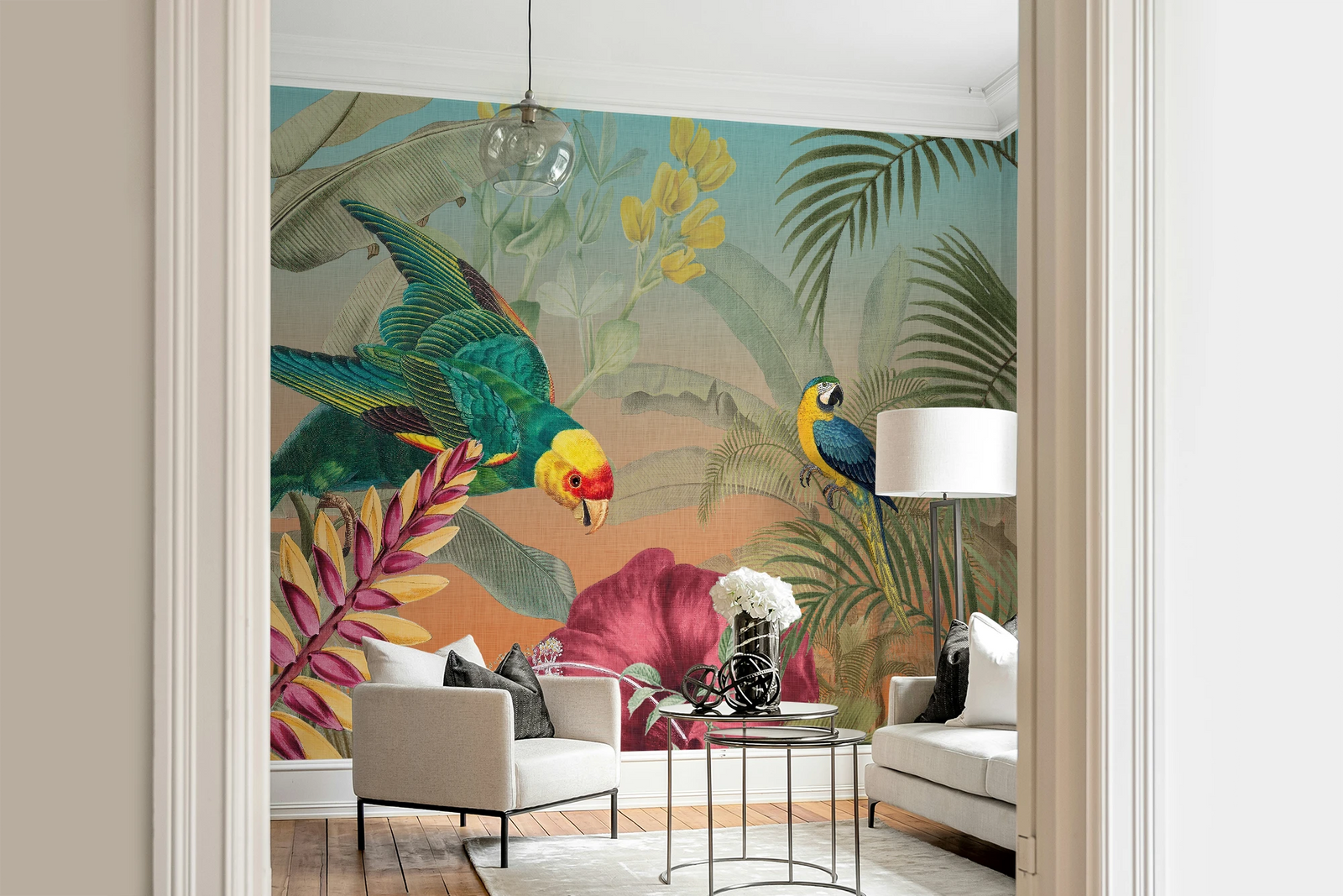 A colorful tropical wallpaper mural featuring parrots, palm leaves, and large pink flowers, shown installed in a modern living room with white sofas, a glass coffee table, and a pendant light.