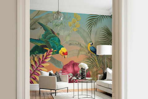 A colorful tropical wallpaper mural featuring parrots, palm leaves, and large pink flowers, shown installed in a modern living room with white sofas, a glass coffee table, and a pendant light.