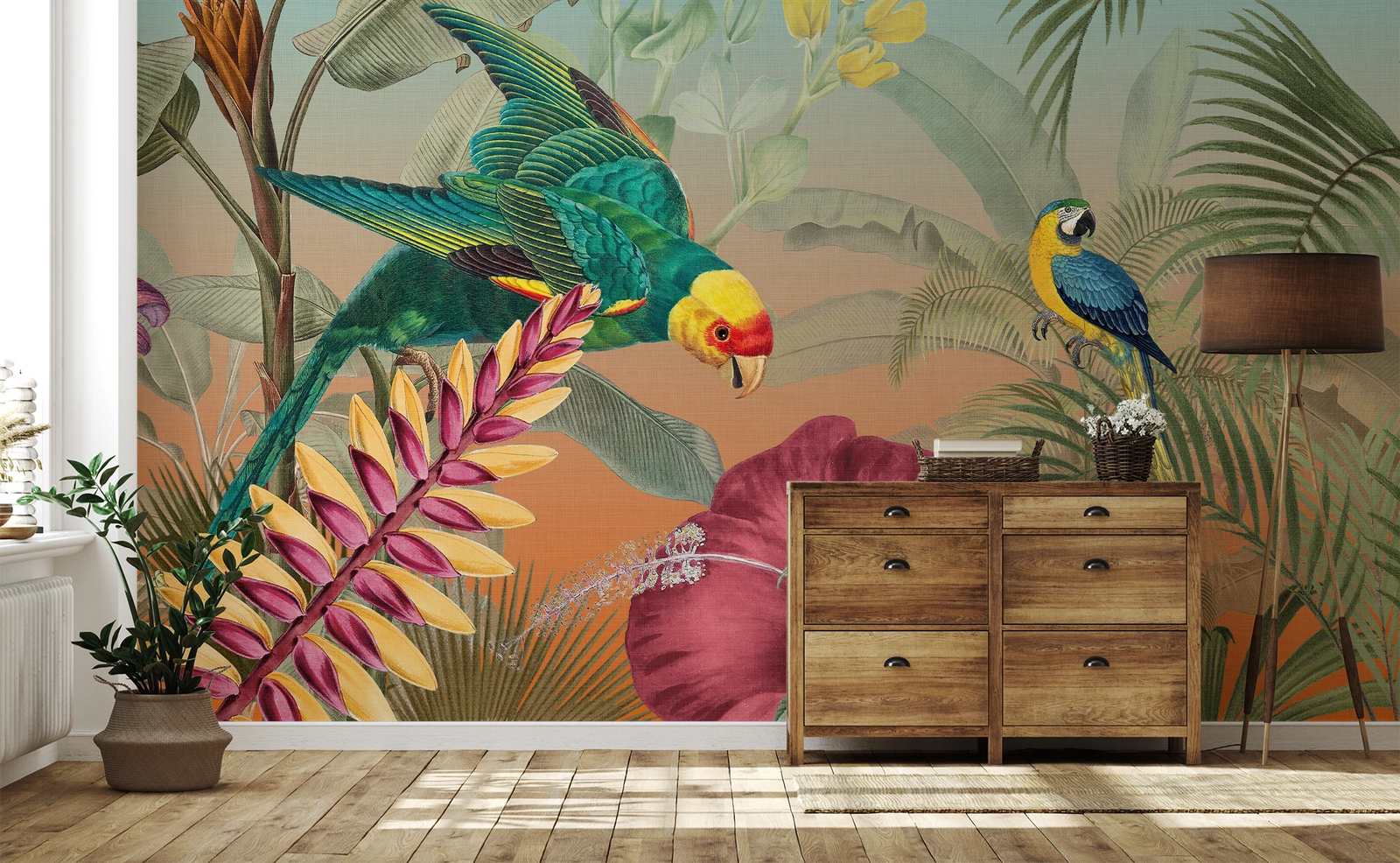 A tropical jungle wallpaper mural featuring a green parrot, a blue-and-yellow macaw, and large palm leaves, shown installed on a wall in a styled room with a wooden dresser, floor lamp, and potted plant.