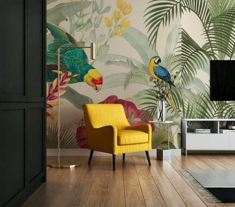 A styled living room featuring a bold tropical wallpaper with parrots and palm leaves, a bright yellow armchair, a gold floor lamp, and a white side table.