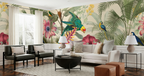 A styled living room featuring a large-scale tropical wallpaper mural with colorful parrots, macaws, and pink flowers on a beige background. The room is furnished with a white sofa, two black armchairs, a black coffee table, side tables with lamps, and brown leather ottomans.