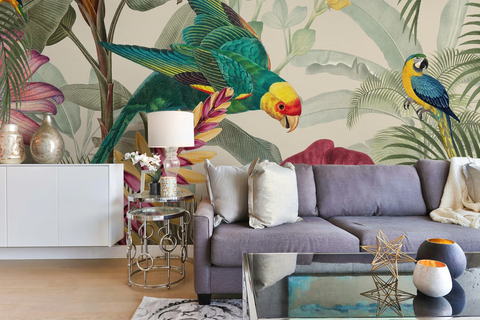 A styled living room featuring a large-scale tropical wallpaper mural with a green parrot, yellow-and-blue macaws, and palm leaves behind a gray sofa with neutral throw pillows.