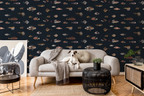 A styled living room featuring dark navy wallpaper with a repeating pattern of small illustrated fish in muted beige, brown, and gray tones. A light gray sofa with a dog lying on it, a black woven side table, and other room decor are visible in front of the wallpaper.