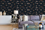 A styled living room featuring a dark navy blue wallpaper with a repeating pattern of various vintage fish illustrations drawn by Marcus Elieser Bloch, in muted beige, brown, and gray tones. In front of the wall is a gray fabric sofa with neutral throw pillows, a white sideboard with decorative vases, a small round metal side table with a lamp, and a glass coffee table in the foreground.