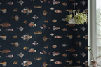 Dark navy wallpaper with a pattern of vintage fish illustrations drawn by Marcus Elieser Bloch, shown in a room setting with a hanging plant and a potted plant near a window.