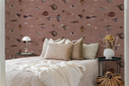 A styled bedroom scene featuring a bed with beige and white bedding, flanked by two black side tables. The wall behind is covered in dusty rose wallpaper with a pattern of vintage fish illustrations drawn by Marcus Elieser Bloch. 