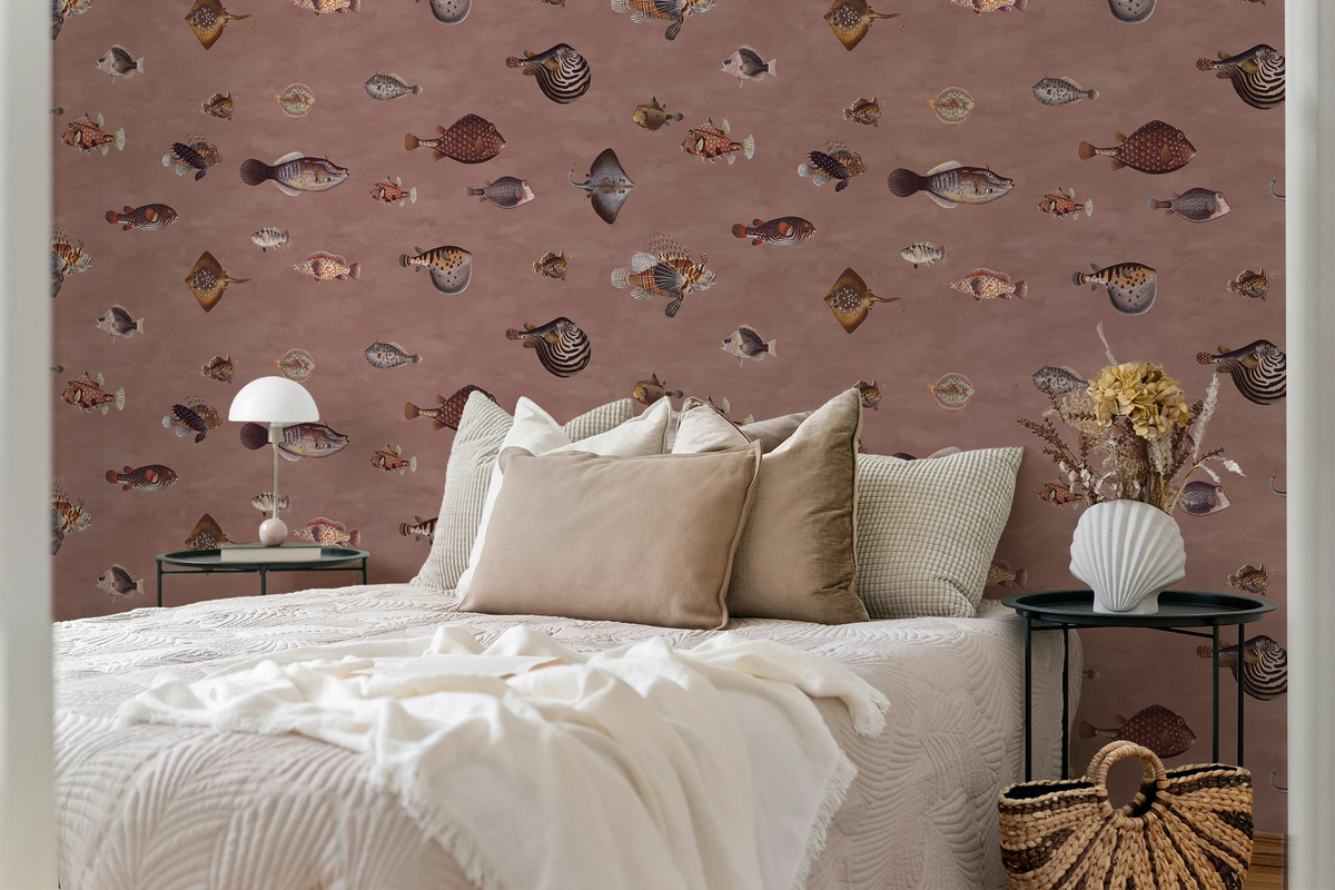 A styled bedroom scene featuring a bed with beige and white bedding, flanked by two black side tables. The wall behind is covered in dusty rose wallpaper with a pattern of vintage fish illustrations drawn by Marcus Elieser Bloch. 