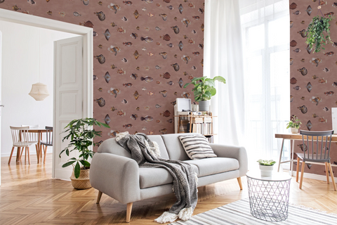 A styled living room featuring terracotta brown wallpaper with a pattern of vintage fish illustrations drawn by Marcus Elieser Bloch, a light gray sofa, wooden floors, and white curtains.