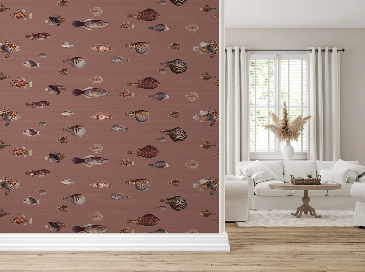 A styled interior room showing a large wall covered in fish-patterned wallpaper on the left made with vintage hand drawn illustrations, with a white sofa, window, curtains, and wood floor visible on the right.
