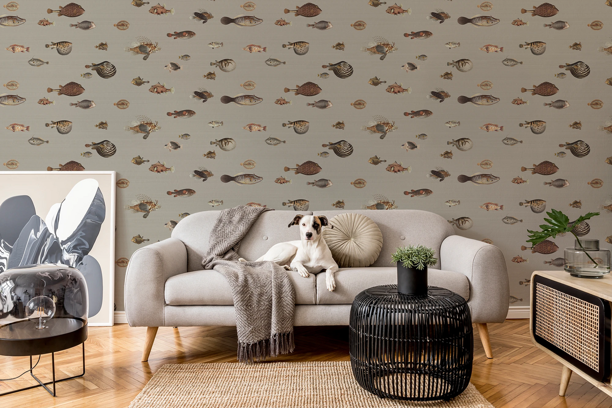 Modern living room with a grey sofa, a dog, art, and a wallpaper with a greige background featuring a pattern of vintage marine life illustrations. 