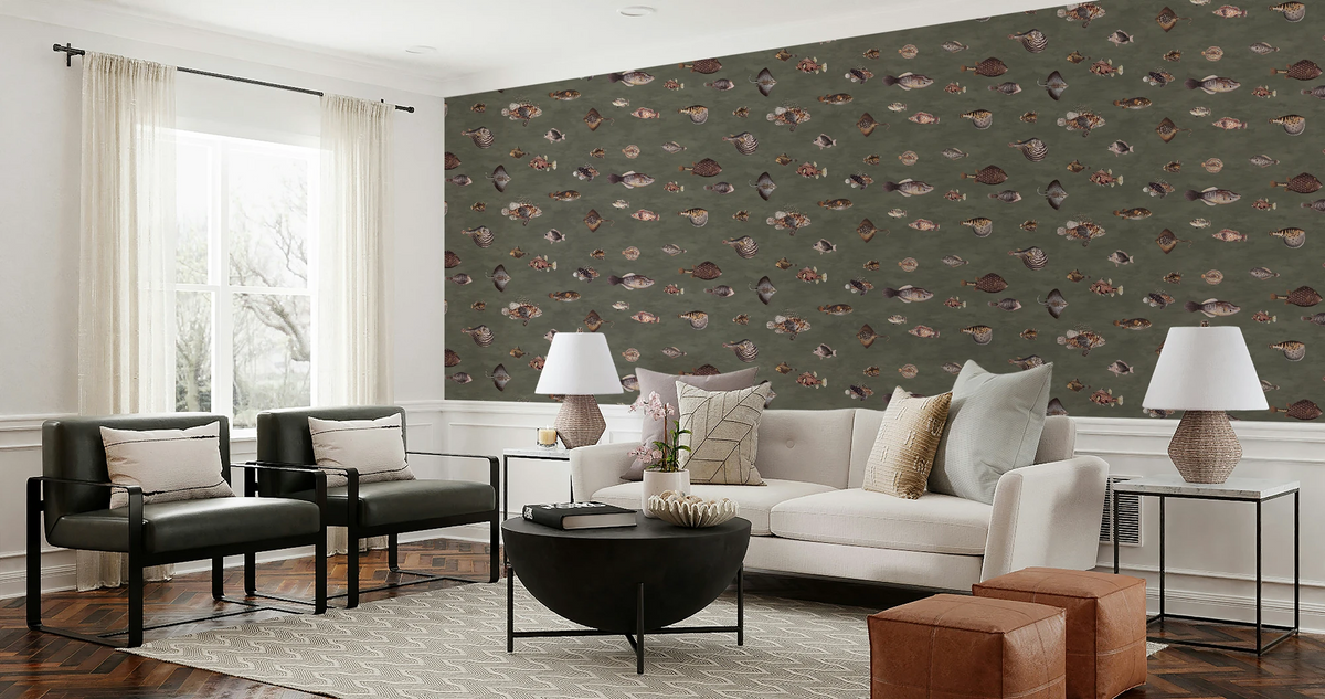 A styled living room featuring a prominent olive green wallpaper with a repeating pattern of small fish and shells, set behind a white sofa, two black armchairs, and modern side tables.