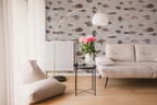 Styled living room with modern furniture, a grey sofa, a floor lamp, a small black side-table with a vase, and a wallpaper with a pattern of vintage fish illustrations drawn by Bloch, on an ivory background. 