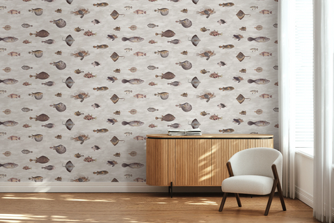 A styled interior room showing wallpaper with a repeating fish pattern on a light background, installed on a wall behind a wooden cabinet and a white armchair near a window.